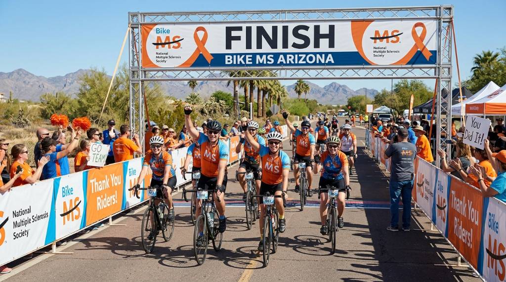 Group of charity cyclists crossing the finish line at Bike MS Arizona with MS Society banners in background
